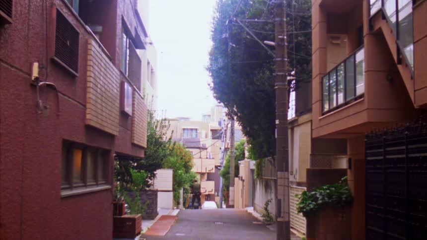 A man pushes a cart in an alley way as another man rides his bike around him