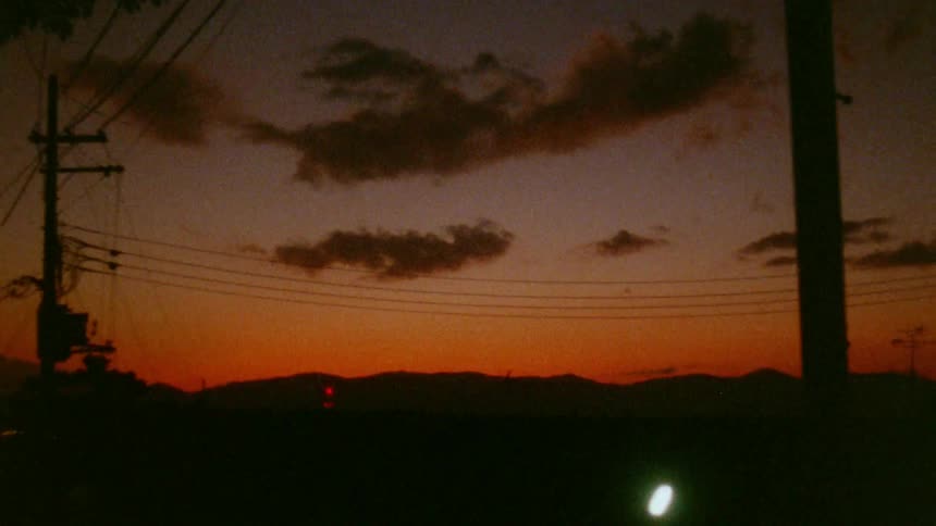A fiery orange sunset paints the sky silhouetting power lines and distant hills