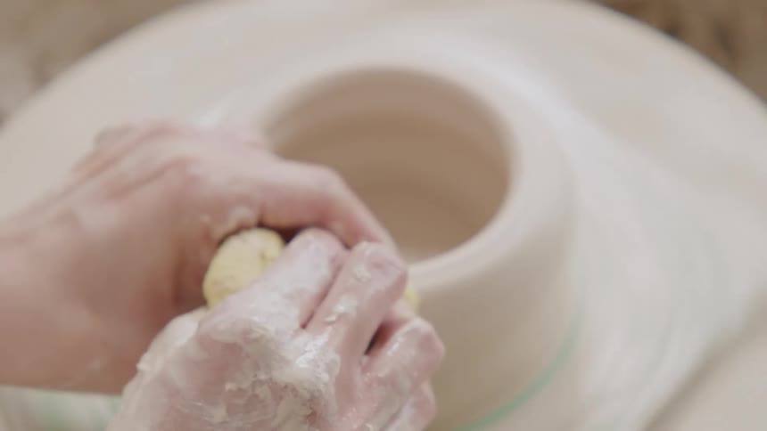A person shapes a clay pot on a pottery wheel hands covered in wet clay