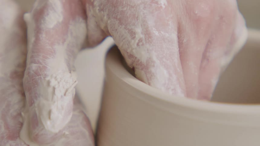 Close up of a pair of hands shaping a clay vase over a turning table