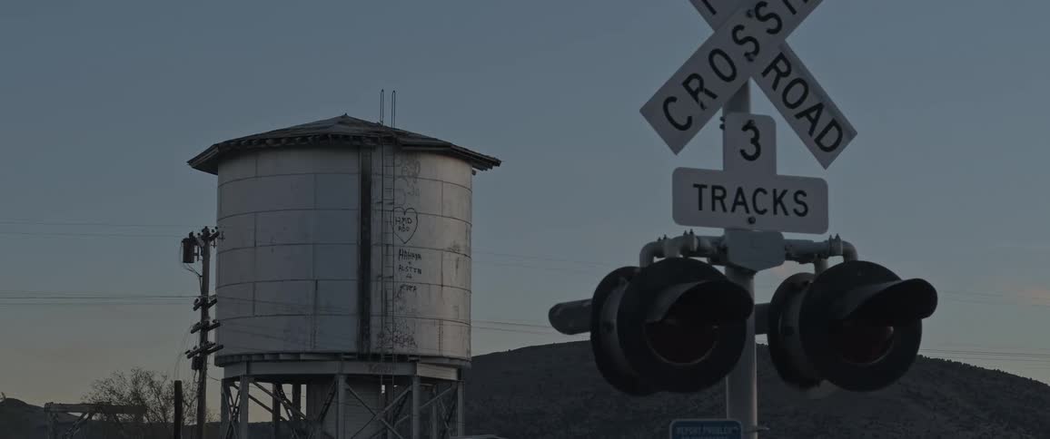 A railroad crossing sign with a water tower in the background situated in a rural area with hills and sparse vegetation