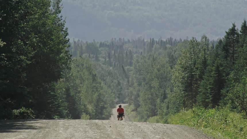 Cyclist riding on a dirt road surrounded by dense forests with treecovered hills in the background in a peaceful natural setting