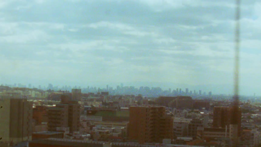 A dense cityscape stretches out into the distance seen from an ascending elevator