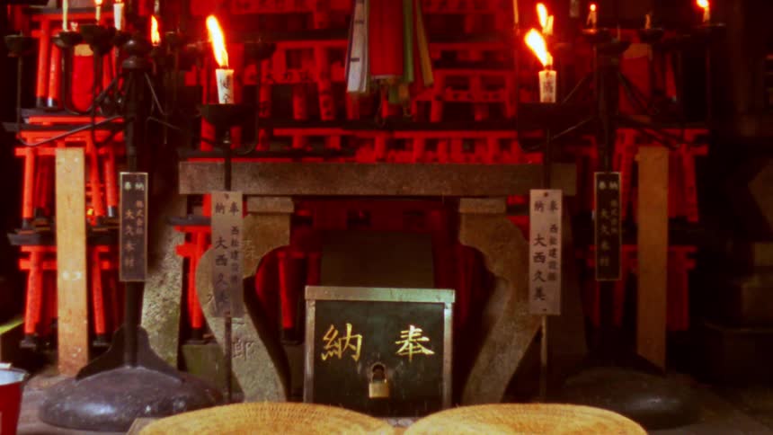 A traditional japanese shrine with lit candles stone structures and numerous red torii gates in the background