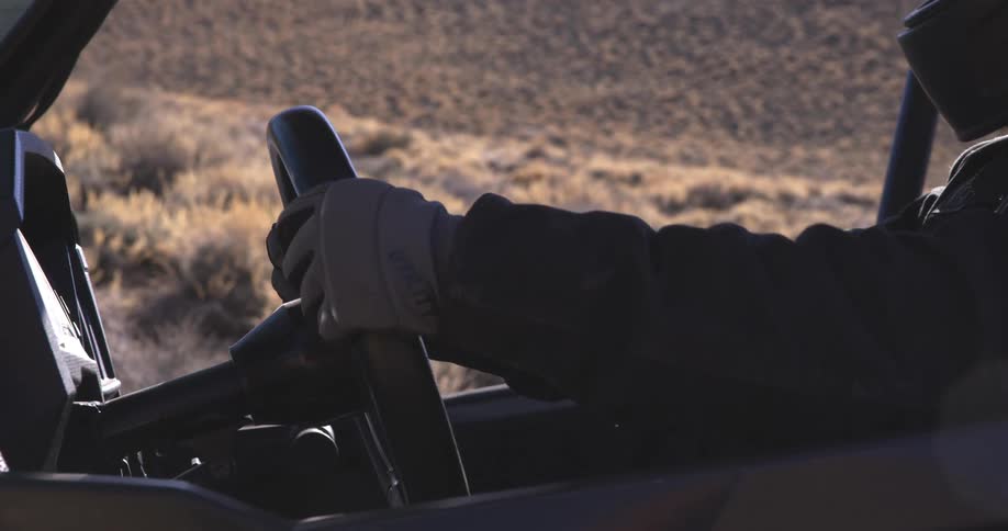A person wearing gloves is gripping the steering wheel of an offroad vehicle with a desert landscape visible in the background