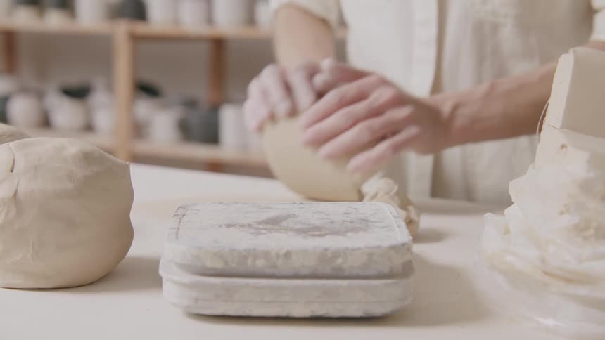 A craftsperson molds clay surrounded by a collection of tools and materials