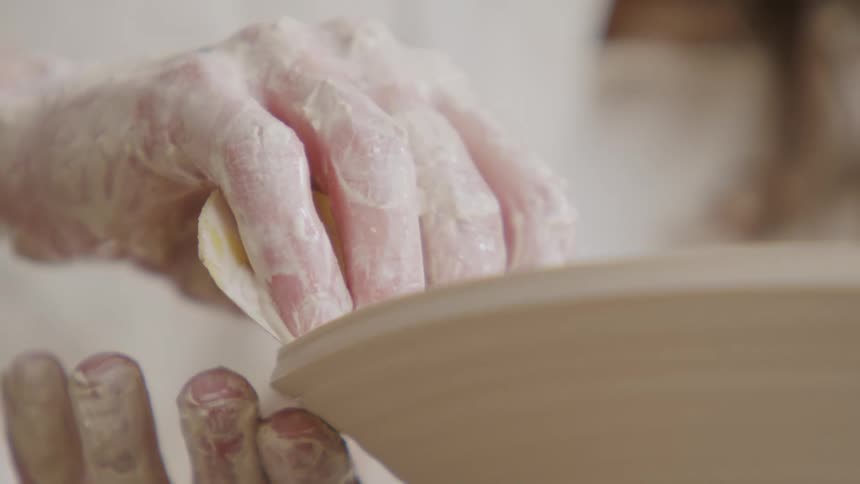A woman uses a shaping tool as she makes pottery