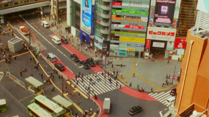 Aerial view of a busy intersection in a japanese city with pedestrians crossing crosswalks vehicles moving around and buildings surrounding