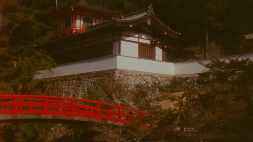 A red bridge leads to a house with a stone foundation