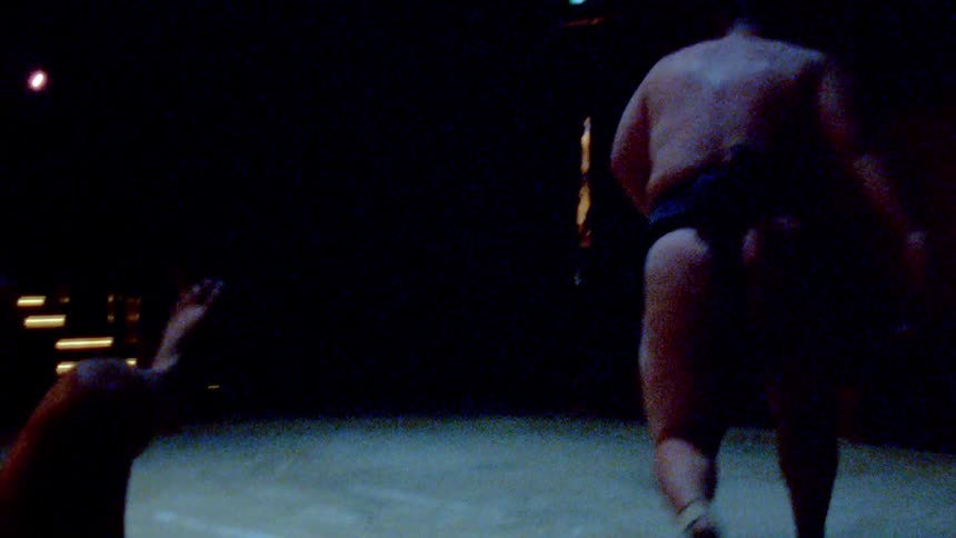 Sumo wrestlers engage in a match on a dimly lit arena
