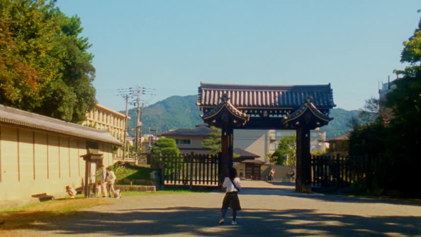 Kids play off to the side in a neighborhood as a woman looks at a pagoda