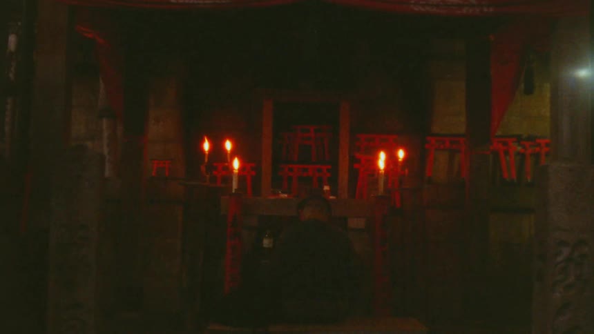 A man is at an altar praying that is only lit by candles