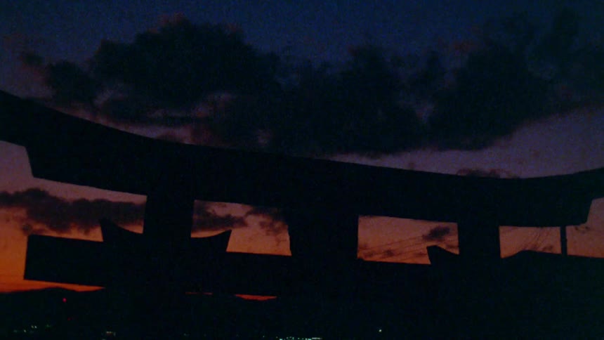 The silhouette of a japanese torii gate stands against a vibrant orange and purple sunset