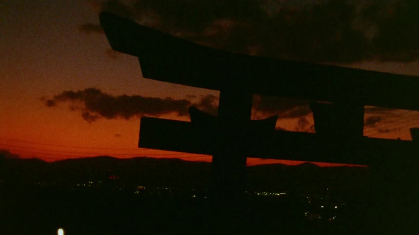 The silhouette of a japanese torii gate stands against a vibrant orange and purple sunset