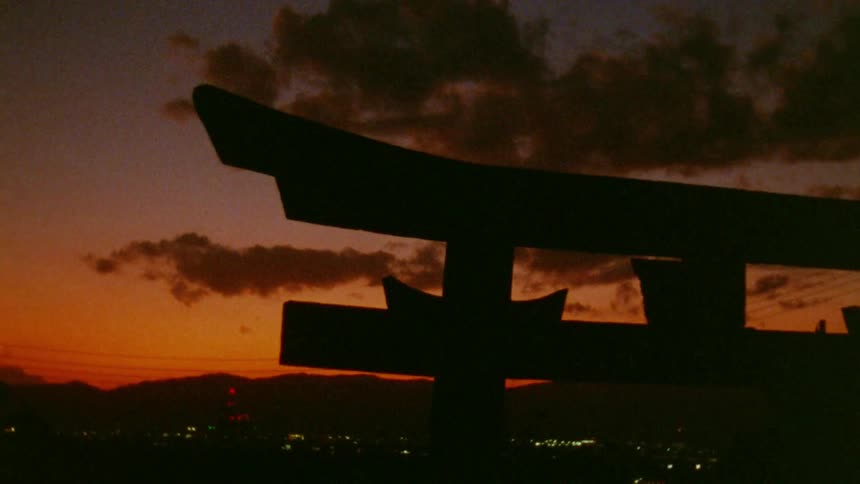 The silhouette of a japanese torii gate stands against a vibrant orange and purple sunset