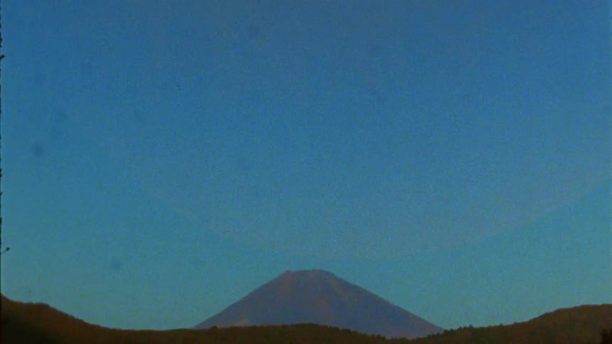 Mount fujis snowcapped peak rises against a clear blue sky with green surroundings below