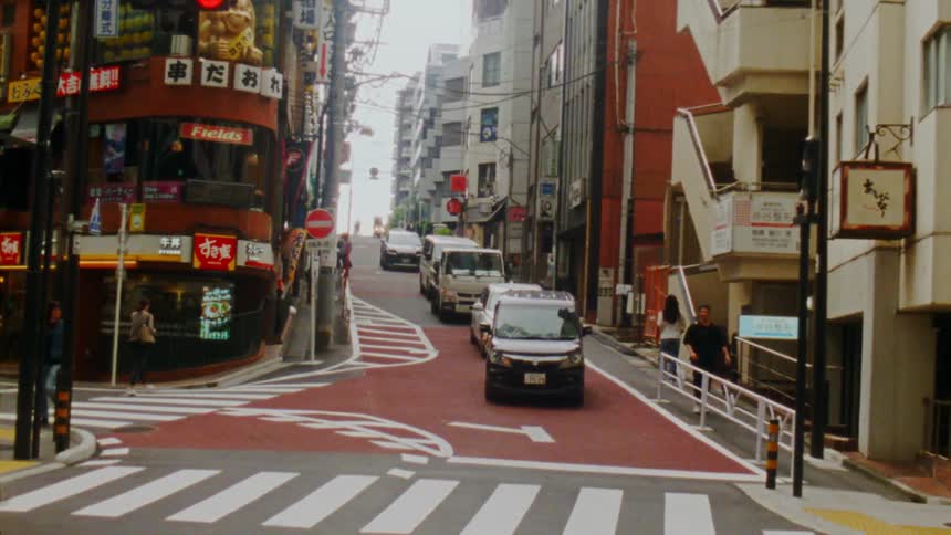 A bustling street in japan with commercial buildings vehicles and pedestrians on a steep incline