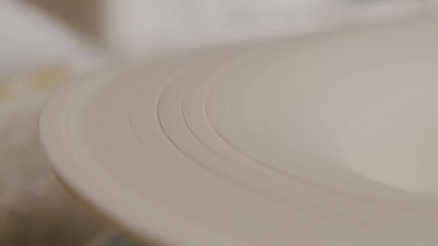 A closeup of a fresh clay plate being turned on a spinning wheel