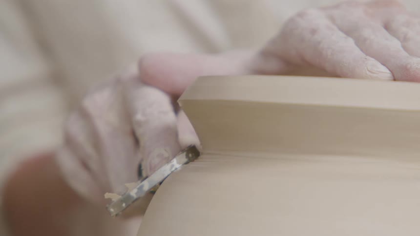 Potter helps shape a clay vessel by shaving parts off with a tool