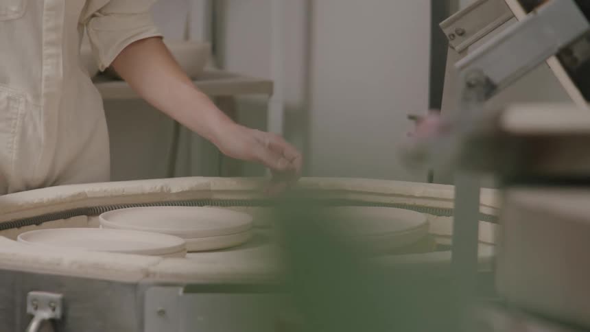 Person working with pottery positioning clay plates on a lathe