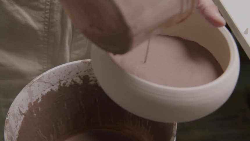 A potter pours a viscous glaze into a ceramic bowl