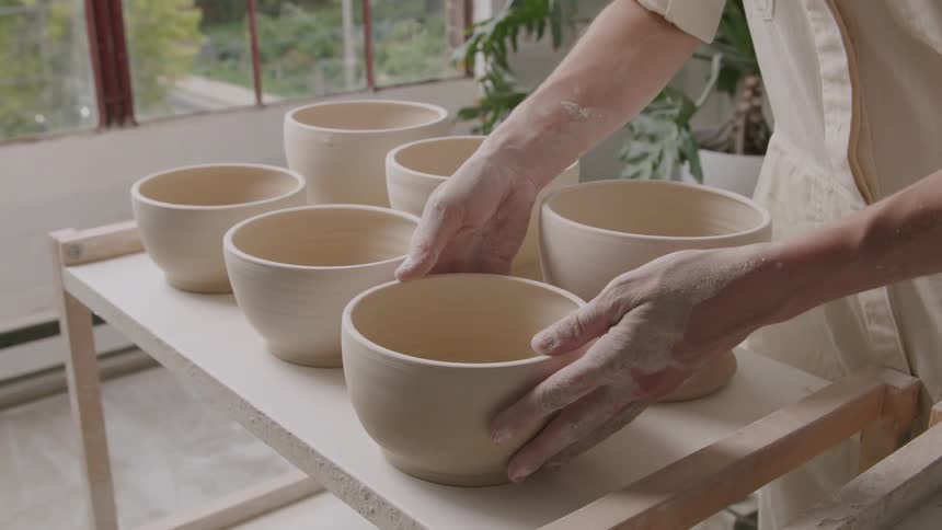 A woman carefully places pottery on a table