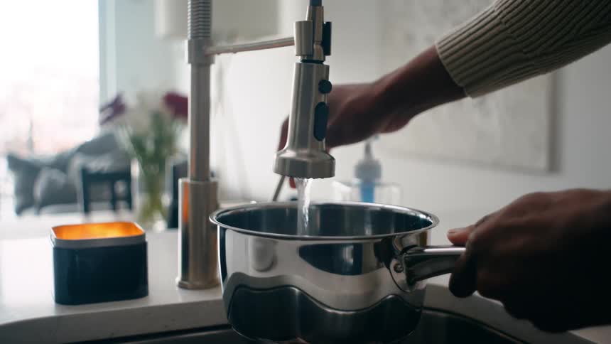 A man fills the pot with water from the sink