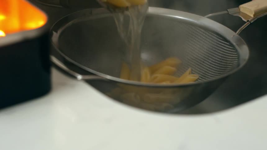 Cooked pasta being poured into a bowl in the sink