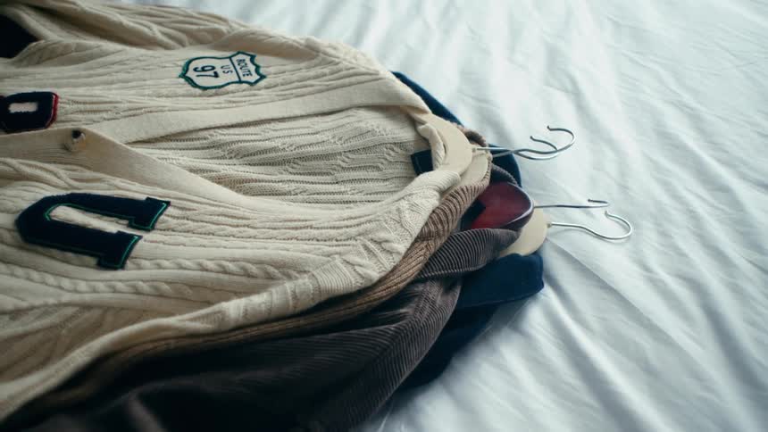 A stack of sweaters with clothes hangers inside placed on a bed