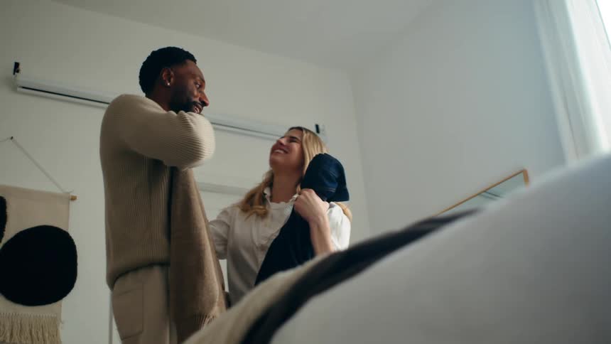 A man and woman are folding clothes in a bedroom smiling and laughing with each other