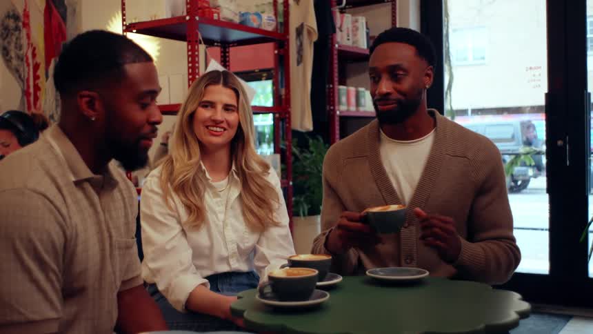 Three friends are sitting around a table in a coffee shop talking and enjoying their coffees