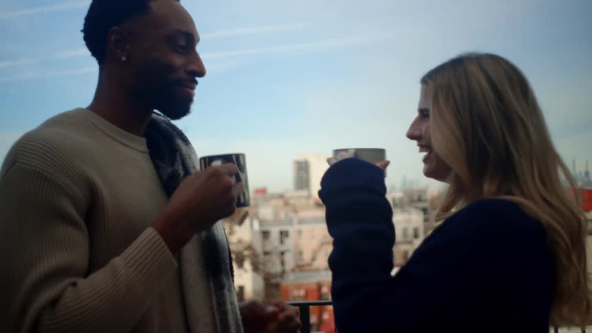 A young couple toasting with tea on a balcony overlooking a city