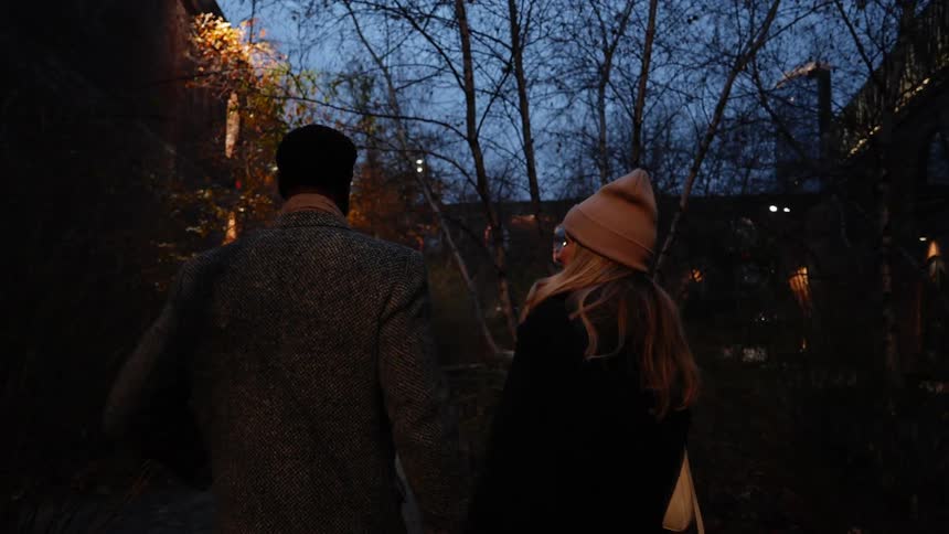 Couple holds hands while walking along the sidewalk near apartment buildings on a winter evening