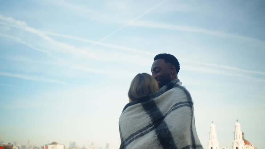 Couple cuddling together wrapped in a blanket outdoors