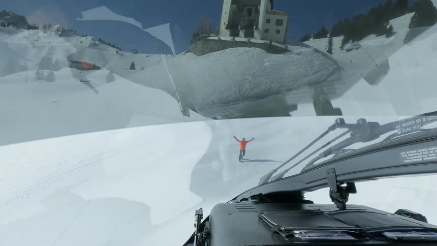 A view from the front window of a vehicle approaching a person in orange clothing standing on a snowwhite ground