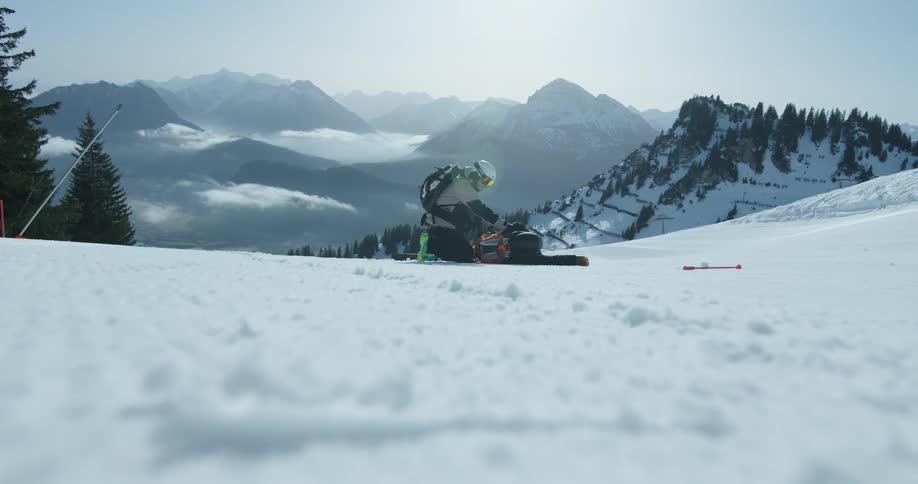 Skier crouches on a snowy slope surrounded by snowcapped mountains and trees