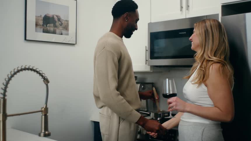 Couple holding hands while cooking on the stove and the woman holds a glass of wine