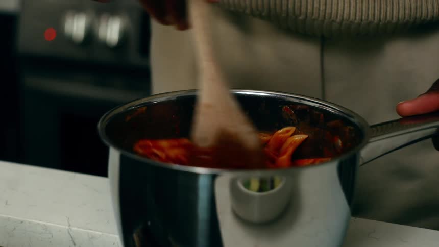 A person is stirring a pot of pasta with tomato sauce
