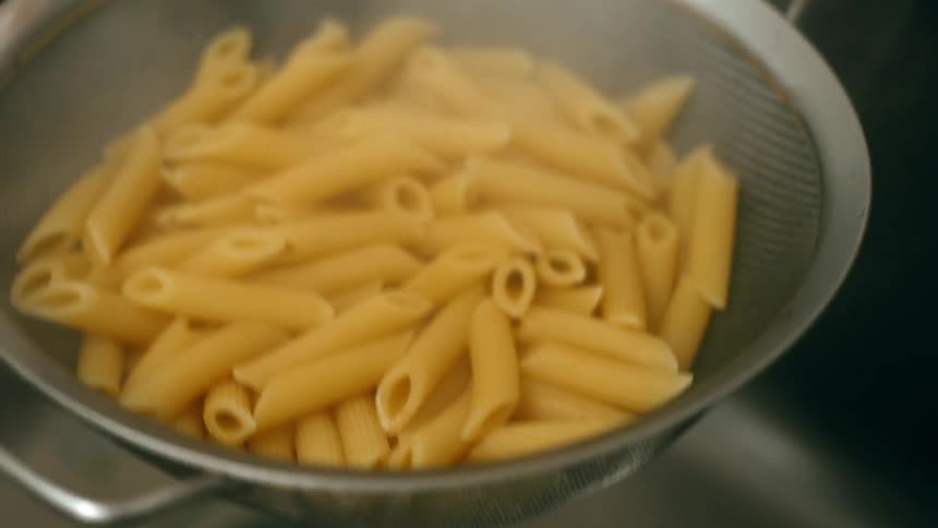 A colander of noodles is being shaken over a sink