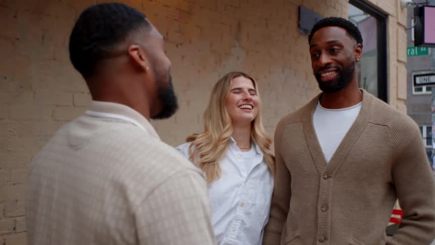 Three people talk in front of a brick wall