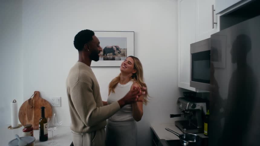 Couple dance and hug while standing in the kitchen of their home