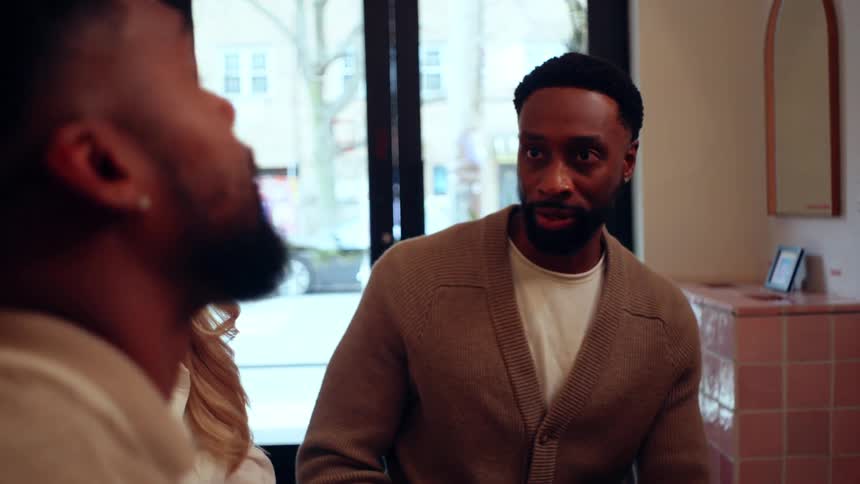 A man in a brown cardigan is engaged in conversation with two other people
