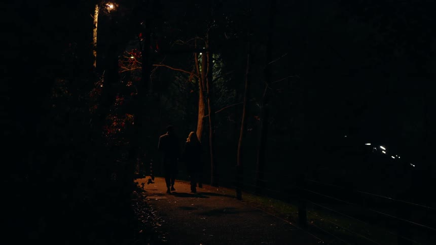 A man and woman walk down the sidewalk in the dark
