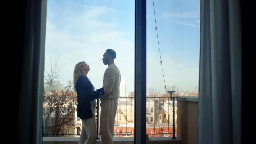 A man and woman are on a balcony talking and hugging