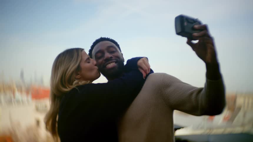 A man and woman are smiling and kissing while taking selfies