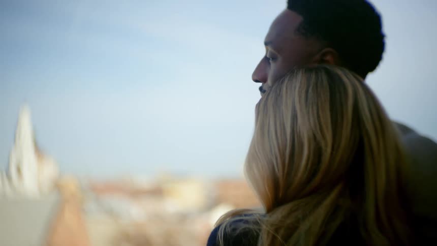 A young couple embraces on a balcony overlooking the city