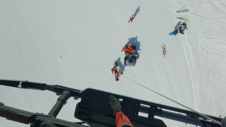 Rescue team on a snowy slope with a stretcher and equipment nearby captured from a helicopter