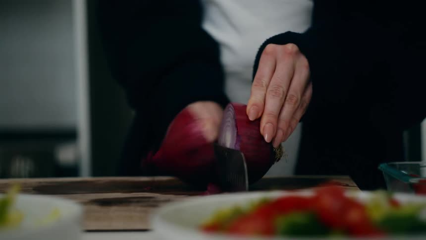 A woman cuts a red onion in half