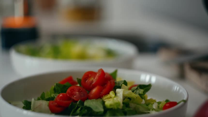 Two people add tomatoes to a bowl while preparing a salad