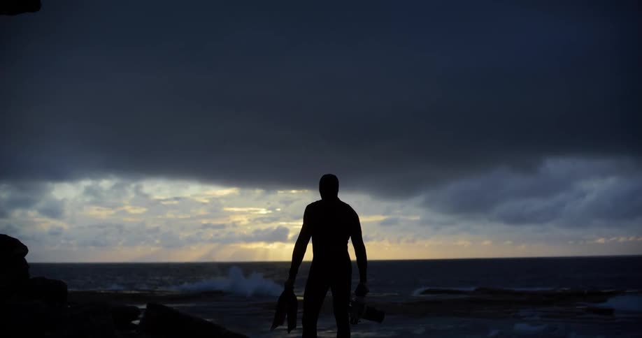 Silhouette of a man in a swimming suit and a rock by the sea
